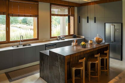 La cocina tiene una gran isla de Dekton con banquetas (Quintana Casa) ideales para desayunar mirando al valle. Lamparas (Imdi). Cortinas (Riel Americano).