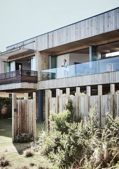 La dueña de casa busca olas desde el living en el primer piso, con baranda de vidrio. Al lado está la suite principal, con baranda y parasol de madera.