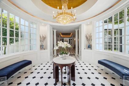 La elegancia de la mansión se refleja en sus detalles arquitectónicos, como los suelos de mármol y piedra, columnas neoclásicas, y candelabros dorados