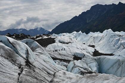 La enorme escala del glaciar se deja ver con las montañas de fondo y un grupo de turistas que lo visitan