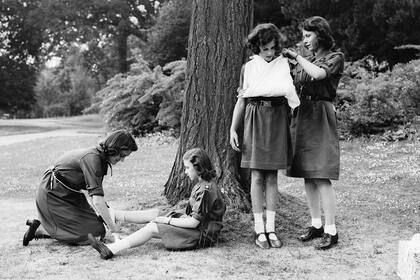 La entonces princesa Isabel coloca el brazo de su amiga Myra Butter en un cabestrillo durante un campamento de guías en Frogmore, Windsor, en abril de 1942. 