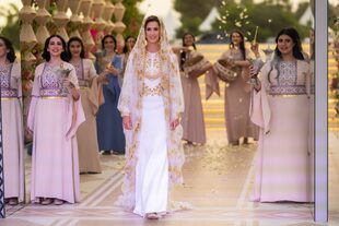 La entrada de la joven arquitecta a los jardines del palacio. Para el gran día eligió un vestido de estilo árabe en tono marfil con bordados dorados de la firma saudí Honayda. El modelo, confeccionado con apliques en 3D, seda e hilos metálicos, combina elementos tanto de Jordania como de Arabia Saudita para celebrar la unión de Rajwa y el príncipe Hussein.