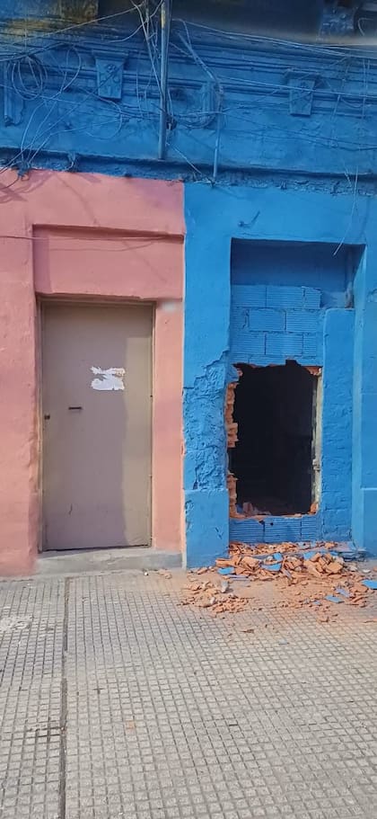 La entrada tapiada de la vivienda en Necochea al 1200, con el hueco abierto en la pared azul y restos de ladrillos sobre la vereda tras el intento de usurpación
