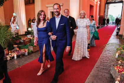 La entrada triunfal fue del brazo de sus hijos: el príncipe heredero Haakon con la princesa Ingrid Alexandra (compuso su estilismo con un vestido azul de Reformation, cartera tejida de la firma italiana Maria La Rosa, sandalias Unisa Shoes y pendientes Sophie Bille Brahe) y MetteMarit (con vestido de The Vampire’s Wife, sandalias Gianvito Rossi y un original clutch firmado por Serpui, con forma de tucán) junto al príncipe Sverre Magnus.