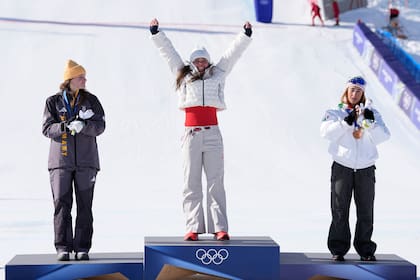 La estadounidense Breezy Johnson celebra tras ganar la medalla de oro en el descenso de esquí alpino femenino junto a la medallista de plata, la alemana Ema Aicher y la medallista de bronce, la italiana Sofia Goggia el domingo 8 de febrero del 2026. (AP Foto/Andy Wong)