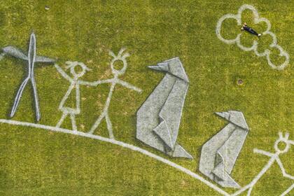 La figura humana del artista Saype dentro de una nube dibujada sobre el césped ayuda a tener una perspectiva de las enormes dimensiones de la obra.