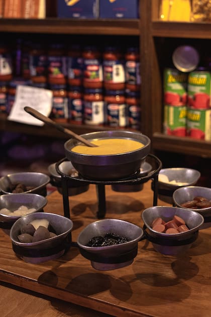 La fondue se acompaña de pan, tomates cherry, salchicha ahumada, papines, pollo, ciruelas, cebollita en vinagre y manzana verde