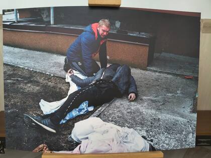 La fotografía de la exposición muestra un civil cargando a un cadáver por las calles de Bucha, Ucrania
