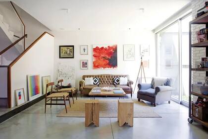 Tacos macizos (Mercadolibre), banquetas de cuero y tiento (Notalo) y mesita con patas de hierro (Quadrat). Detrás de la biblioteca de fenólico y hierro diseñada por Romina, se preservó la pared de ladrillos original de la casa. La alfombra de yute es de Ikea.