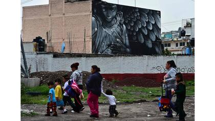 La gente camina cerca de un edificio decorado con un mural del artista mexicano Tenxor