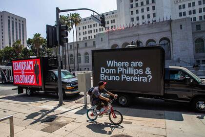 La gente camina junto a un camión con mensajes sobre el periodista británico Dom Phillips y el especialista en asuntos indígenas brasileño Bruno Pereira, que están desaparecidos en la selva amazónica, frente al Ayuntamiento de Los Ángeles en Los Ángeles, California, el 8 de junio de 2022. - Líderes del Norte y Sudamérica se reúnen en Los Ángeles para la novena Cumbre de las Américas. (Photo by Apu GOMES / AFP)