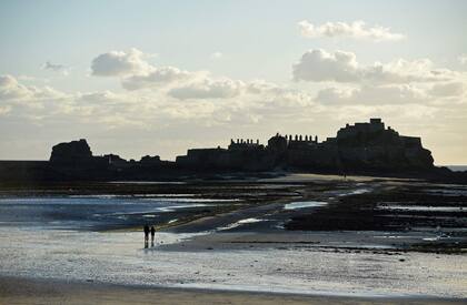 La gente camina por la arena durante la marea baja hacia el Castillo de Elizabeth en St Aubins's Bay, desde St Helier, en la isla británica de Jersey