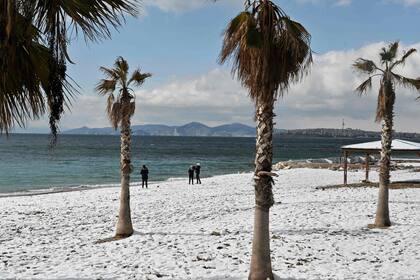 La gente camina por una playa cubierta de nieve en Atenas el 25 de enero de 2022