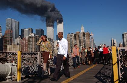 La gente camina sobre el puente de Brooklyn mientras el World Trade Center arde el 11 de septiembre de 2001 después de que dos aviones secuestrados se estrellaran contra las torres gemelas en la ciudad de Nueva York.