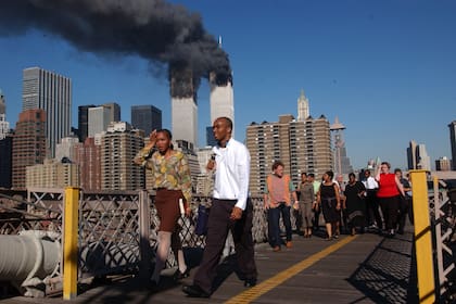 La gente camina sobre el puente de Brooklyn mientras el World Trade Center arde