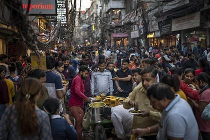 La gente come comida callejera mientras los compradores abarrotan un mercado en Nueva Delhi, India