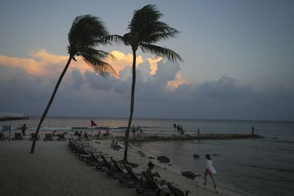La gente descansa en la playa mientras se pone el sol antes de la llegada prevista del huracán Beryl, en Playa del Carmen, México