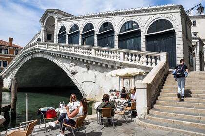 La gente disfruta de una bebida en la terraza de un café junto al puente de Rialto y el Gran Canal de Venecia el 18 de mayo de 2020