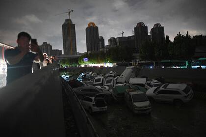 La gente mira los autos sumergidos en un paso subterráneo luego de las fuertes lluvias en Zhengzhou, en la provincia china de Henan