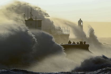 La gente observa cómo las olas chocan contra el malecón en Porthcawl, Gales del Sur, el 18 de febrero de 2022 cuando la tormenta Eunice trae fuertes vientos en todo el país.