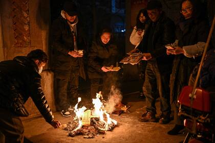 La gente quema ofrendas, para rendir homenaje a los miembros de la familia que fallecieron el año pasado, en la víspera del Año Nuevo Lunar en Wuhan, en la provincia central china de Hubei, el 21 de enero de 2023. 