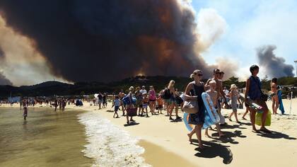 La gente sale de la playa con sus pertenencias mientras un incendio arde un bosque detrás de ellos en Bormes-les-Mimosas, sureste de Francia.