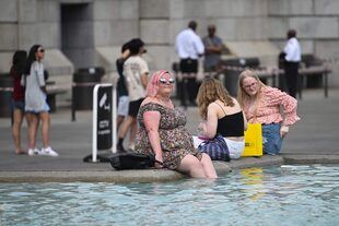 La gente se refresca con los pies en el agua de la fuente de Trafalgar Square, en el centro de Londres, el 13 de julio de 2022, durante una ola de calor. (Photo by JUSTIN TALLIS / AFP)
