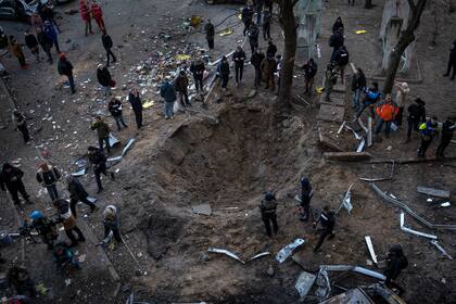 La gente se reúne alrededor de un cráter creado por una bomba que dañó gravemente edificios y coches en Kiev, Ucrania, el domingo 20 de marzo de 2022