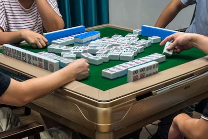 La gente se reúne alrededor de una mesa de mahjong, tradicional juego de fichas chino. El mahjong es especialmente popular en las regiones de Sichuan y Chongqing, donde se ha convertido en un pasatiempo cultural distintivo, disfrutado a menudo por amigos y familiares