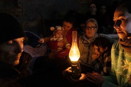 La gente se sienta alrededor de una lámpara en un refugio antibombas en Mariupol, Ucrania