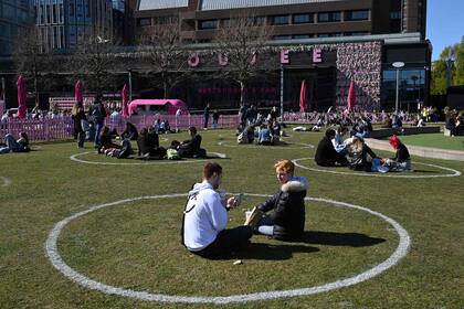 La gente se sienta en círculos pintados en el césped para ayudar a mantener el distanciamiento social, en el complejo comercial al aire libre Liverpool One, en el noroeste de Inglaterra