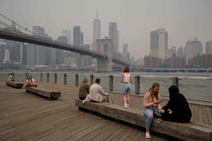 La gente se sienta en el parque del puente de Brooklyn mientras el humo de los incendios forestales en Canadá causan condiciones de niebla en la ciudad de Nueva York 