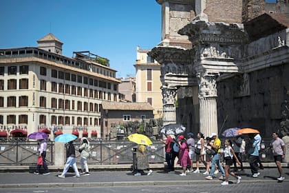 La gente usa paraguas cuando hace calor para protegerse del sol mientras caminan frente al Foro de Augusto, en Roma