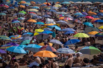 La gente usa sombrillas para protegerse del sol en la playa en un día caluroso y soleado en Barcelona, España, el viernes 15 de julio de 2022.