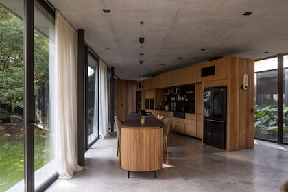 La isla de ocho metros (Muc Muebles) funciona como espacio de trabajo y punto de encuentro familiar. Con extremos curvos en madera maciza, tapa de Dekton ‘Domoos’ y patas que la elevan del piso, logra un aspecto liviano y elegante.