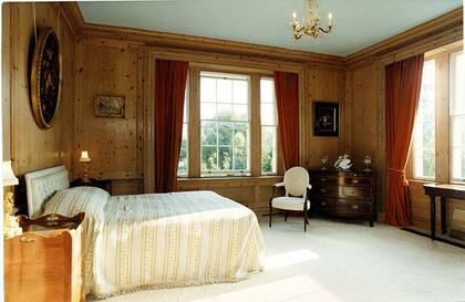 El dormitorio principal lleva paneles de madera en las paredes, que tienen colgados dos cuadros con marcos de bronce y alfombras color crema