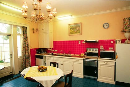 En esta enorme casa, la cocina tiene paredes amarillas con azulejos rojos y el suelo de baldosas azules. Los armarios son blancos con mesadas de madera y tiene una mesa circular de madera en el centro de la habitación
