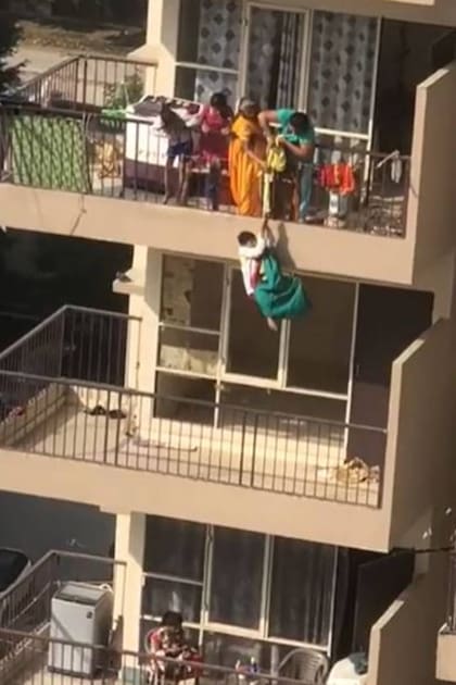 La madre y la abuela del niño tiran del sari para hacerlo subir nuevamente a su balcón