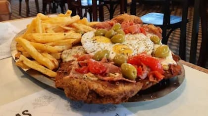 La milanesa gigante se sirve con queso, panceta, morrón y huevo frito