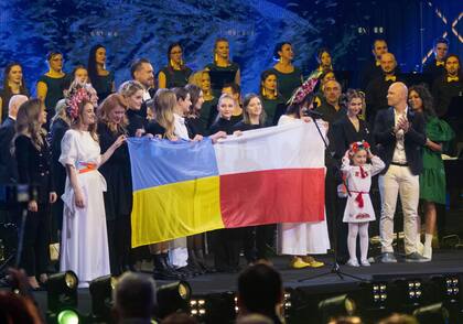 La niña de siete años Amellia Anisovych, refugiada de Ucrania, sostiene su tocado mientras se encuentra junto a una bandera polaca en el final de un concierto para recaudar fondos en Lodz, Polonia, el domingo 20 de marzo de 2022.