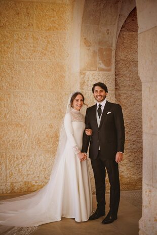 La novia llevó un traje de líneas minimalistas, con mangas largas, escote cuadrado cubierto con encaje, cuello a la base y amplia falda con cola, de Dior. Lo acompañó con una tiara estilo fringe rematada con diamantes –a juego con los pendientes –, que sujetaba el velo decorado con motivos florales y más encaje.