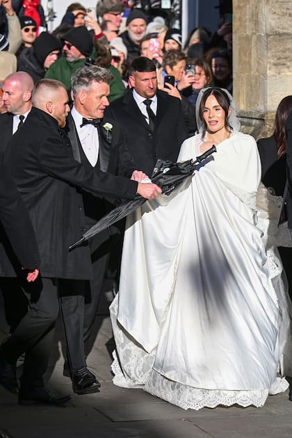 La novia lució una capa en color marfil a través de la cual se pudo espiar algo de su vestido de novia: un diseño clásico en seda y encaje