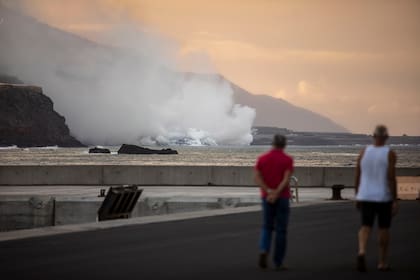 Personas miran la columna de humo mientras la lava del volcán Cumbre Vieja llega al Océano Atlántico