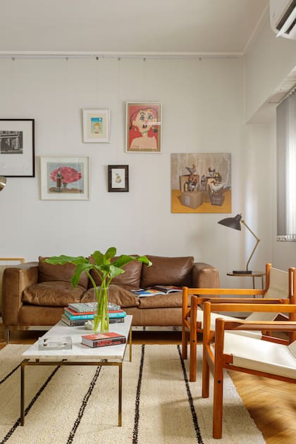 La pared reúne un conjunto ecléctico: fotografía enmarcada de Ignacio Sourrouille, cuadro de Germán Wendel, acuarela de un gato de la dueña de casa y las gallinas de Claudia Melo. Sillones en madera y cuero color natural.
