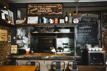 La parrilla a la vista de los comensales rodeada de carteles fileteados y una pizarra con las sugerencias del día
