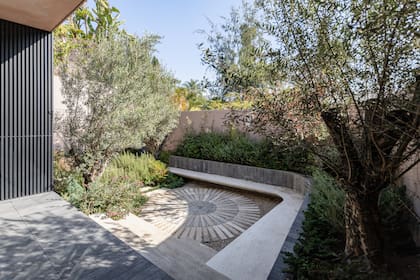 La plaza circular, ya integrada al jardín, se revela como un espacio de transición y permanencia, donde la geometría de las losas dialoga con la vegetación y acompaña el recorrido cotidiano del exterior.