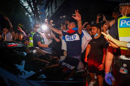 La policía intenta contener a los partidarios del serbio Novak Djokovic mientras rodean un automóvil que sale de las oficinas de su equipo legal