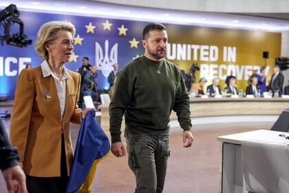 La presidenta de la Comisión Europea, Ursula von der Leyen, con una bandera de Ucrania en la mano, camina junto al presidente del país, Volodymyr Zelenskyy, durante una cumbre entre la UE y Ucrania, en Kiev, Ucrania, el 2 de febrero de 2023. (Oficina de prensa de la Presidencia de Ucrania vía AP)
