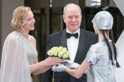 La princesa Charlene –en la foto junto a su marido, el príncipe Alberto II– optó por uno de sus diseños favoritos, el vestido capa con un hombro al descubierto. Firmado por Elie Saab, cumplió con la temática de la gala: plateado y salpicado de brillantes cristales