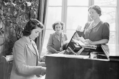 La princesa Isabel toca el piano mientras su madre, la reina Isabel, y la princesa Margarita observan en el Royal Lodge del Castillo de Windsor, Inglaterra, el 11 de abril de 1942. (Photo by Studio Lisa/Getty Images)